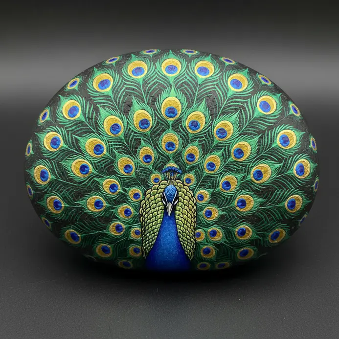 A peacock painted on a rock with metallic blue and gold accents