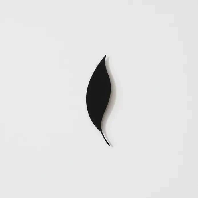 Minimalist black paper leaf cutout mounted on a white wall