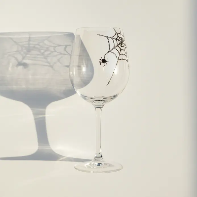 A wine glass drawing with a spiderweb tucked into one upper corner of the bowl and a tiny spider nearby.