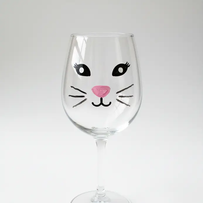 A wine glass sketch with a small animal face centered on the bowl and whisker lines extending to each side.