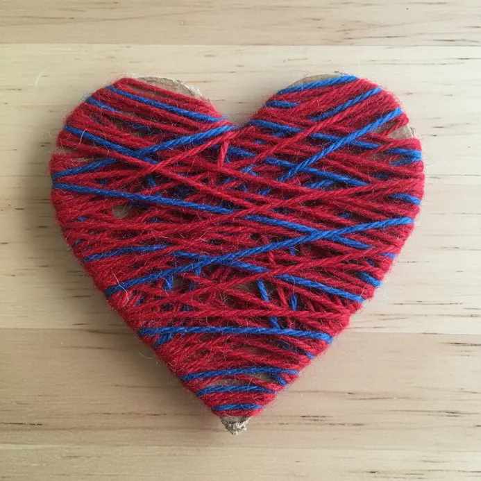 A thick cardboard heart shape tightly wrapped in bright red and orange yarn.