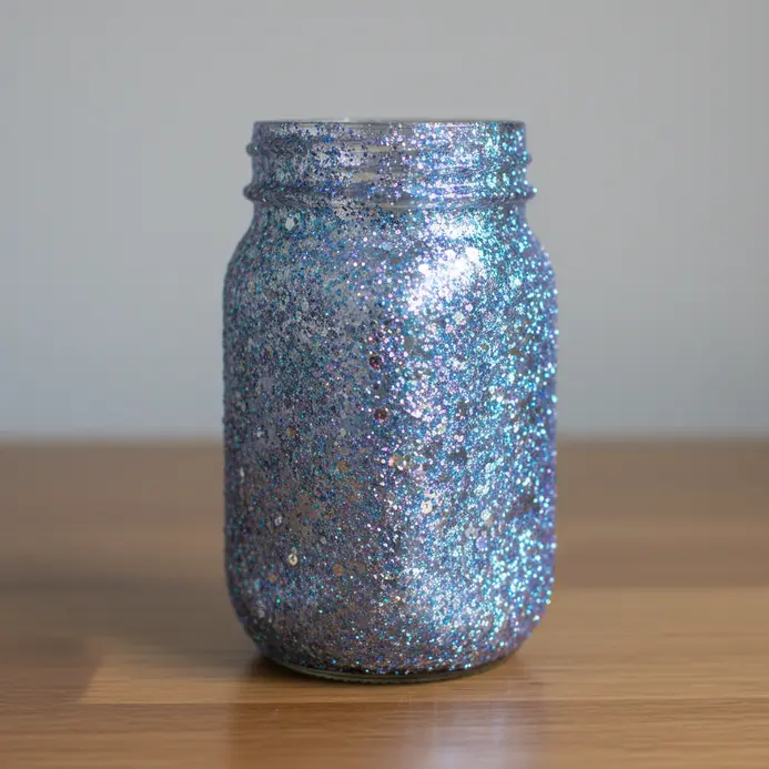 A glass jar coated in thick silver glitter acting as a desk storage container.
