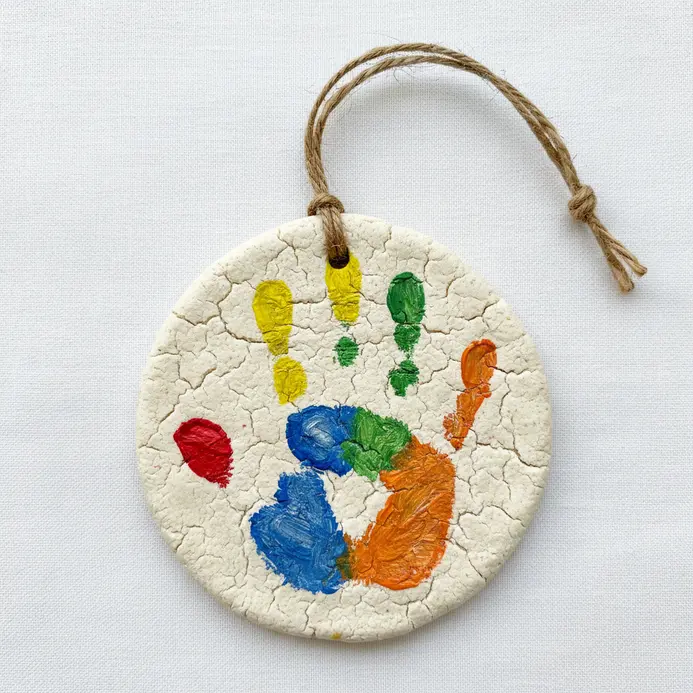 Round salt dough ornaments pressed with child handprints and painted with blue and pink details on twine.