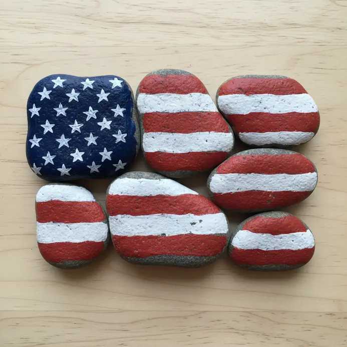 A group of smooth rocks painted with red and white stripes and a blue star field.