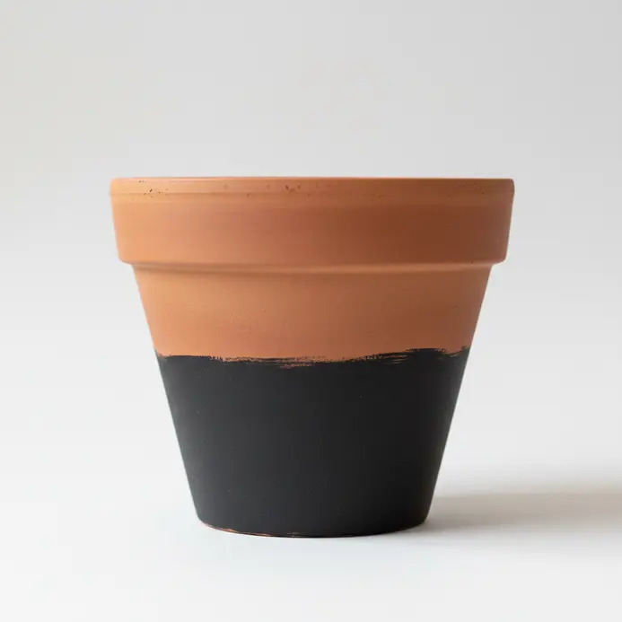 A minimalist terracotta pot painted with a bold matte black color block on its lower half.