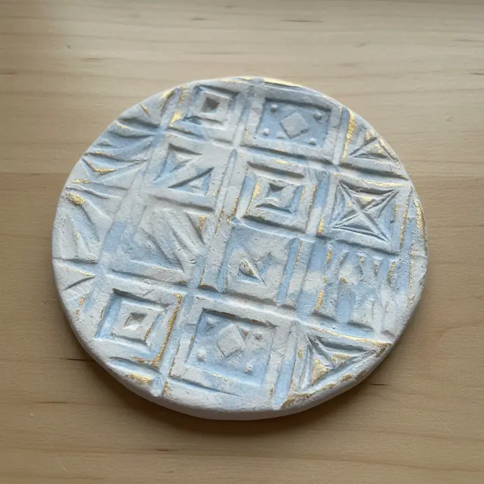 A white air dry clay ornament with textured patterns made by pressing objects into the surface.