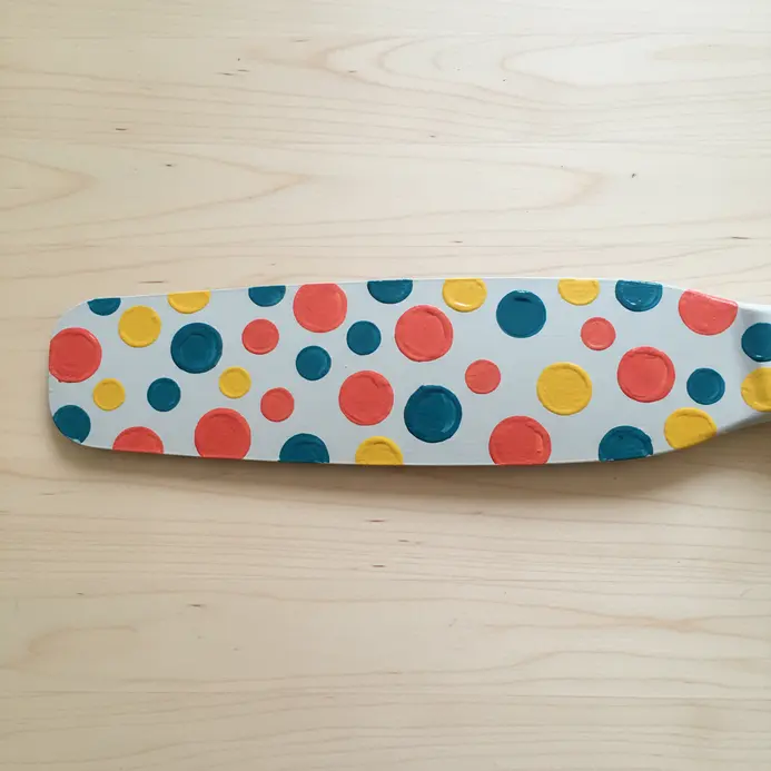A light grey fan blade decorated with scattered, brightly colored painted dots in various sizes.