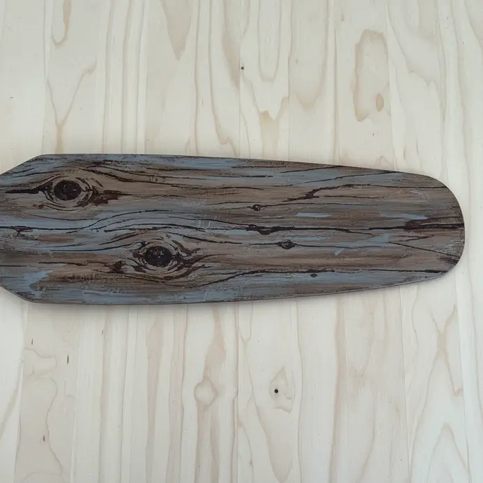 A fan blade with layered brown and grey paint, graining tools used to mimic aged wood planks.