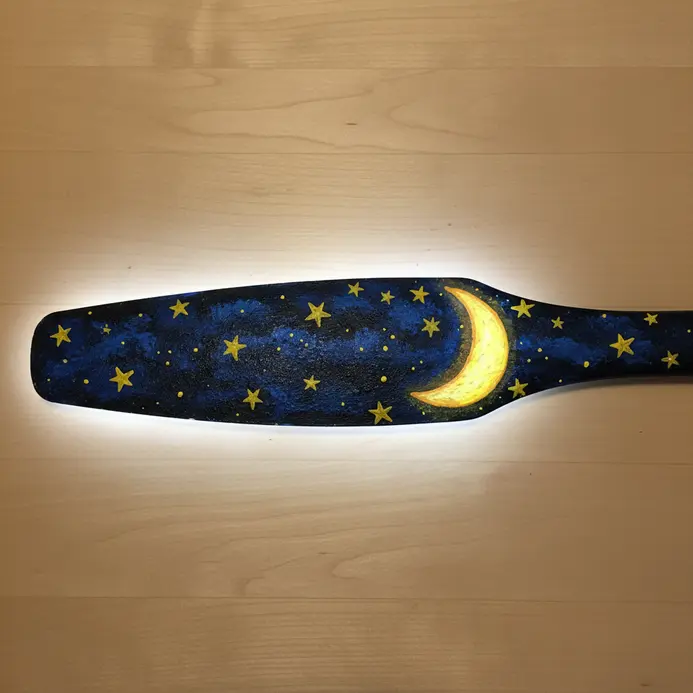 A dark blue fan blade painted with yellow stars and a crescent moon, using glow-in-the-dark paint.