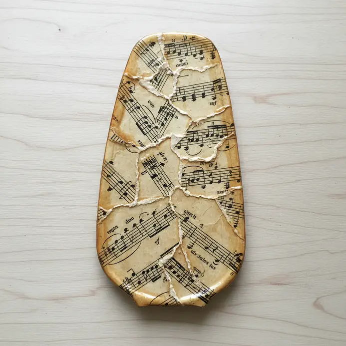 A fan blade layered with fragments of old musical scores sealed with decoupage glue for a cohesive finish.