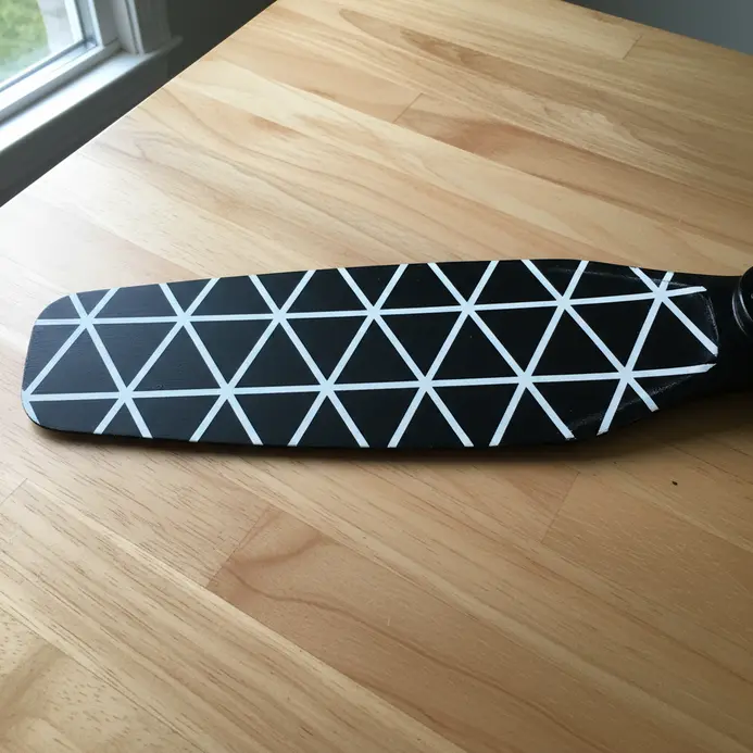 A black fan blade featuring a repetitive pattern of sharp, interconnected triangles stenciled in white.