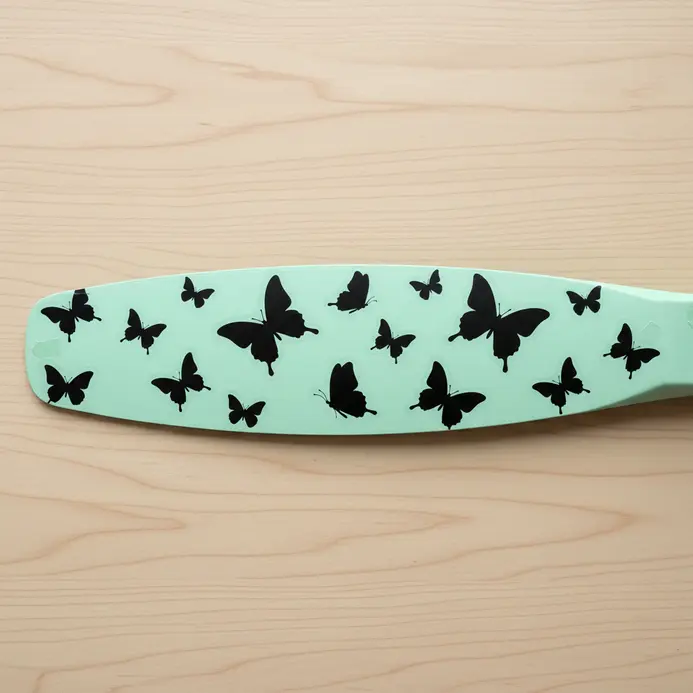 A pale green fan blade adorned with a scattering of black vinyl butterfly decals in various sizes.