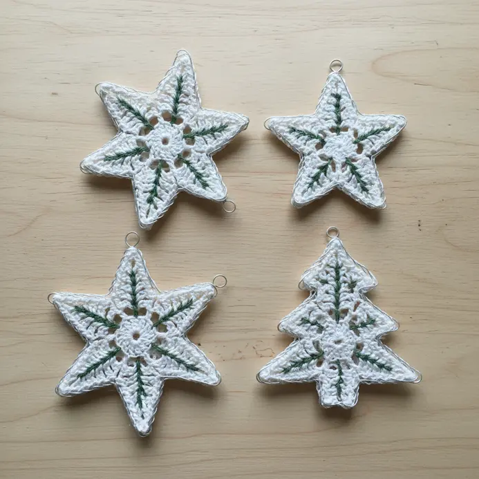 Several stiffened white lace doilies shaped into star and snowflake ornaments hanging on tree branches.