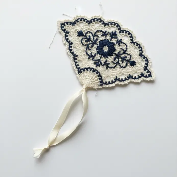 A small, fan-shaped piece cut from a lace doily with a ribbon tail, marking a page in a book.