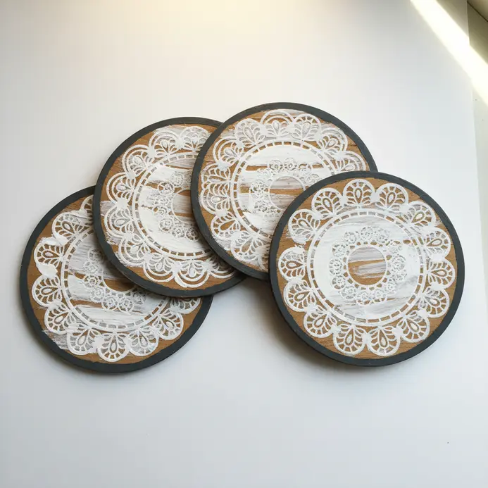 A set of four round wood coasters with a white lace doily pattern painted on each.