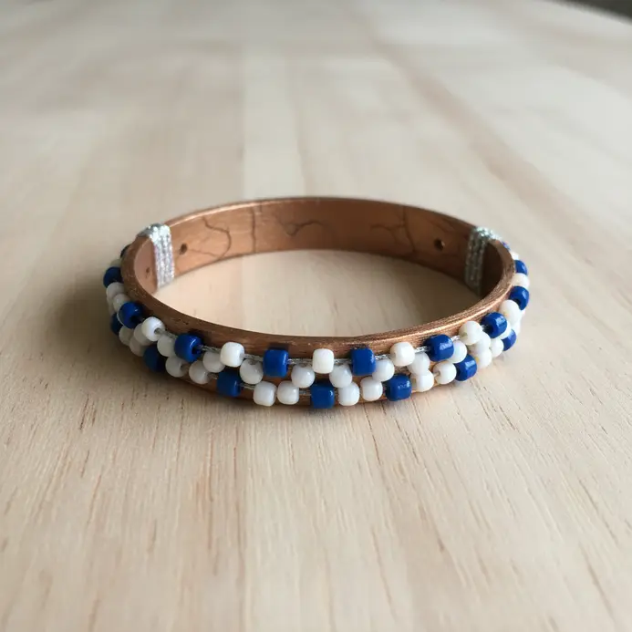A circular bracelet formed by soaking and bending a popsicle stick, decorated with beads and glitter.