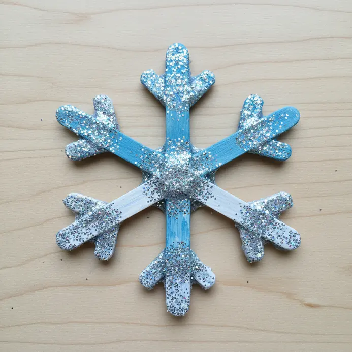 Several six-pointed snowflake ornaments made by gluing popsicle sticks together, painted white and coated in glitter.