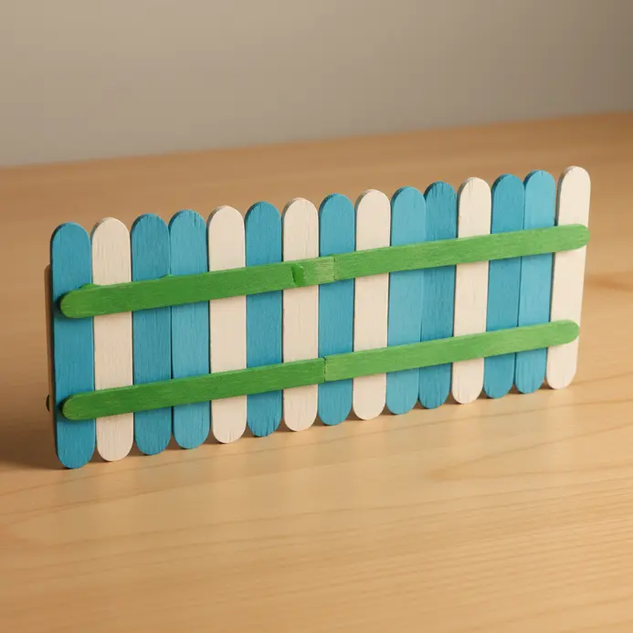 A tiny picket fence made from evenly spaced, white-painted popsicle sticks connected by two horizontal rails.