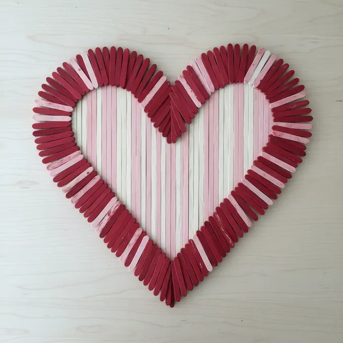 A large heart shape constructed by gluing popsicle sticks together, painted in shades of red and pink.