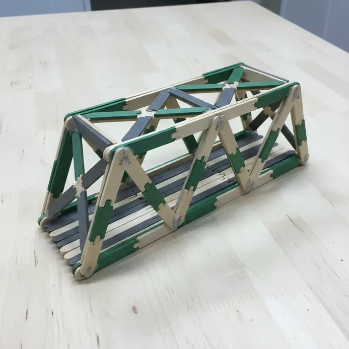 A sturdy, triangular-truss bridge model constructed entirely from notched and glued popsicle sticks.