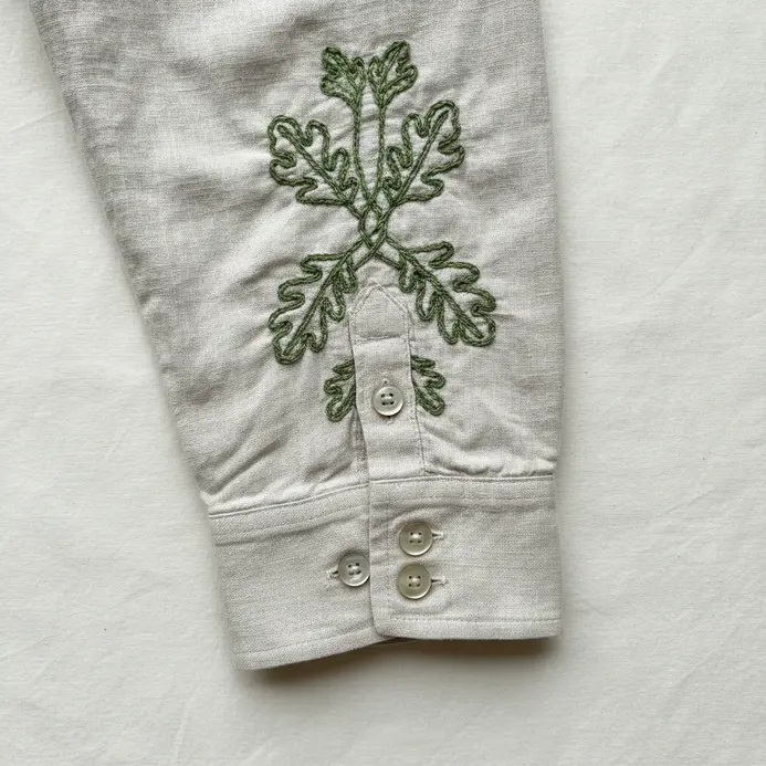 The cuff of a light linen shirt featuring small, precise embroidered initials.