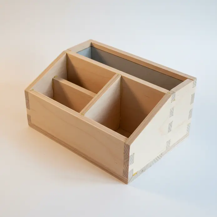 A minimalist desk organizer with angular compartments for pens and notebooks, made from light wood.