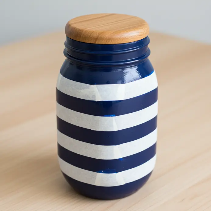 A glass jar painted with alternating wide stripes of navy blue and bright white.