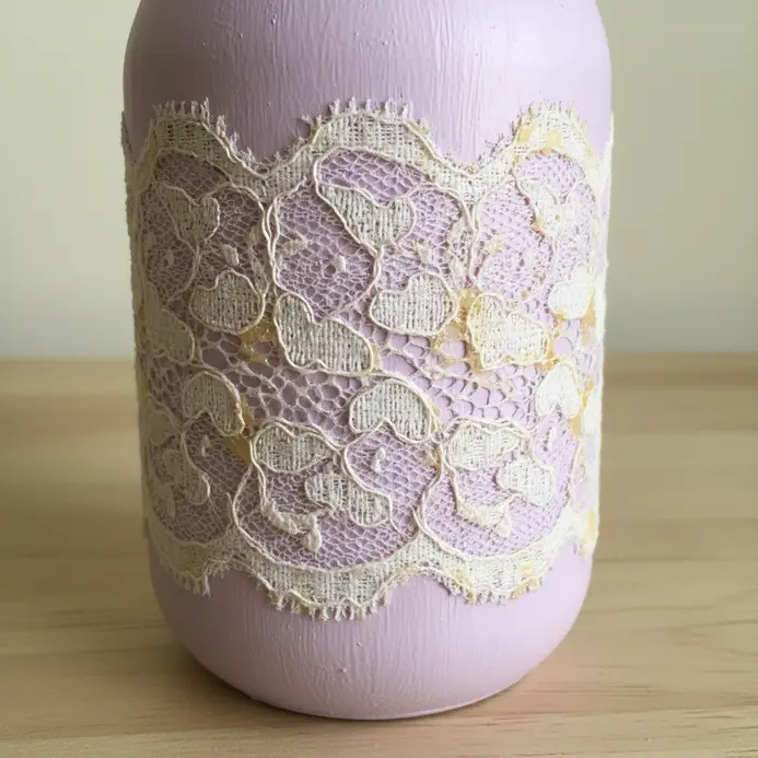A lavender-painted mason jar with a piece of white lace glued around its center.