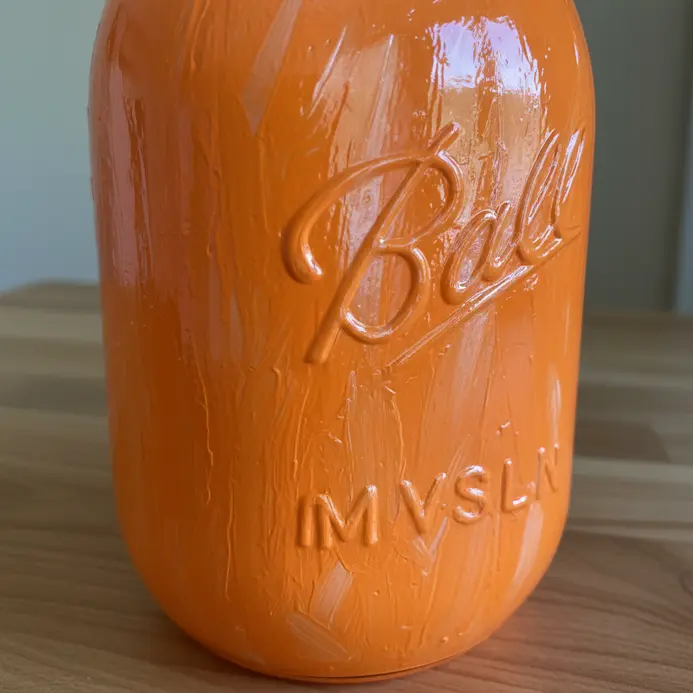 A vibrant, glossy orange painted mason jar sitting in bright sunlight.