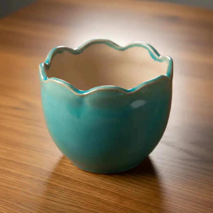 A medium-sized clay planter with an irregular, undulating rim that mimics ocean waves.