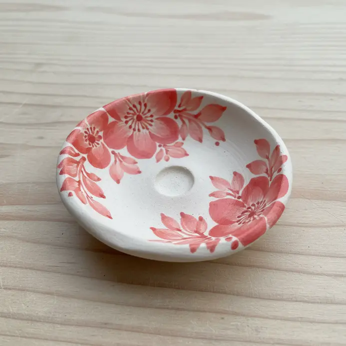A tiny, shallow pinch pot decorated with a detailed painted floral pattern for holding incense.
