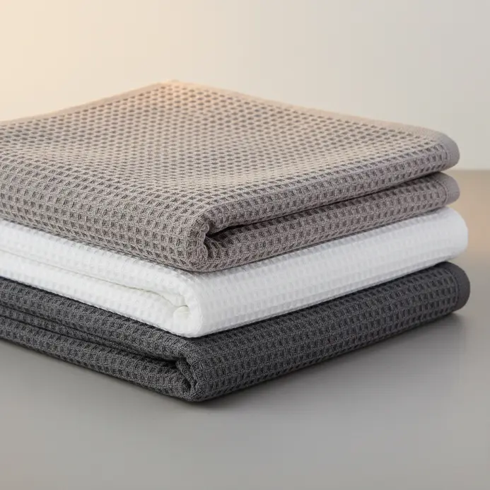 Neatly folded bath towels with a distinctive waffle knit texture in a soft grey hue.