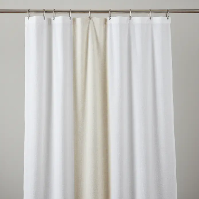 An oversized white fabric shower curtain with a subtle woven texture hanging from a curved shower rod.