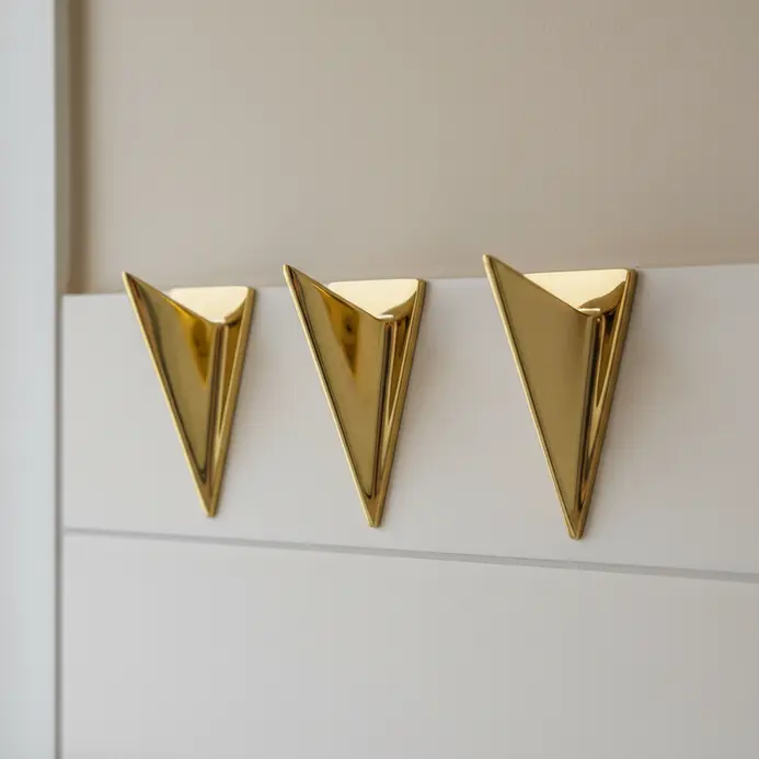 A set of three wall hooks in a geometric triangle shape and a gold finish, holding robes and towels.