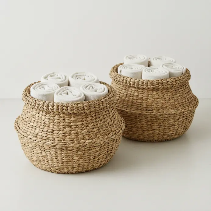 A pair of textured woven seagrass baskets stacked neatly on a bathroom floor, holding rolled towels.