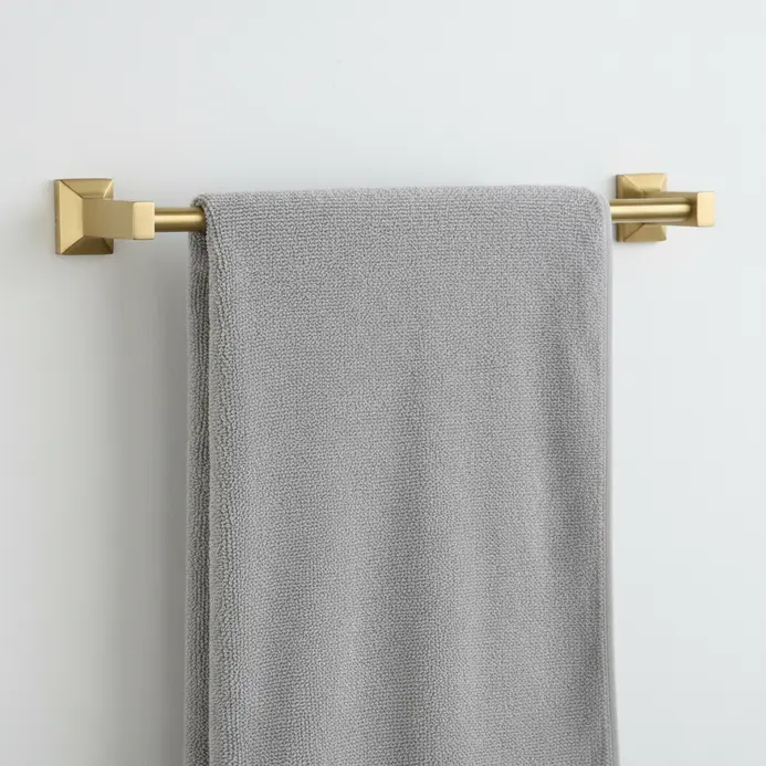 A warm-toned brushed gold towel bar holding fluffy white and grey bath towels against subway tile.