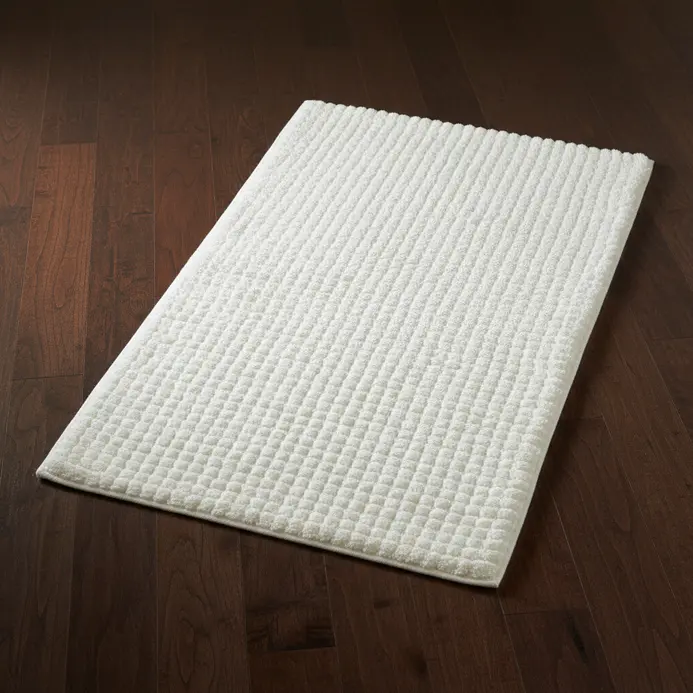 A thick, textured white cotton bath rug with a high pile lying in front of a bathtub.