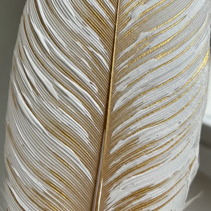 A white feather with thin, parallel gold stripes painted along its central shaft.