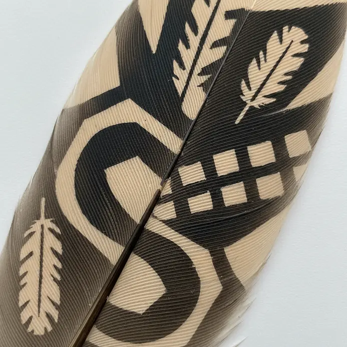 A tan feather covered in a pattern of irregular black spots, mimicking an animal print.