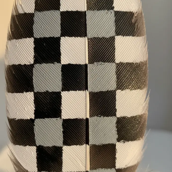A feather is covered in a small-scale, even checkered pattern using only black and white paint.