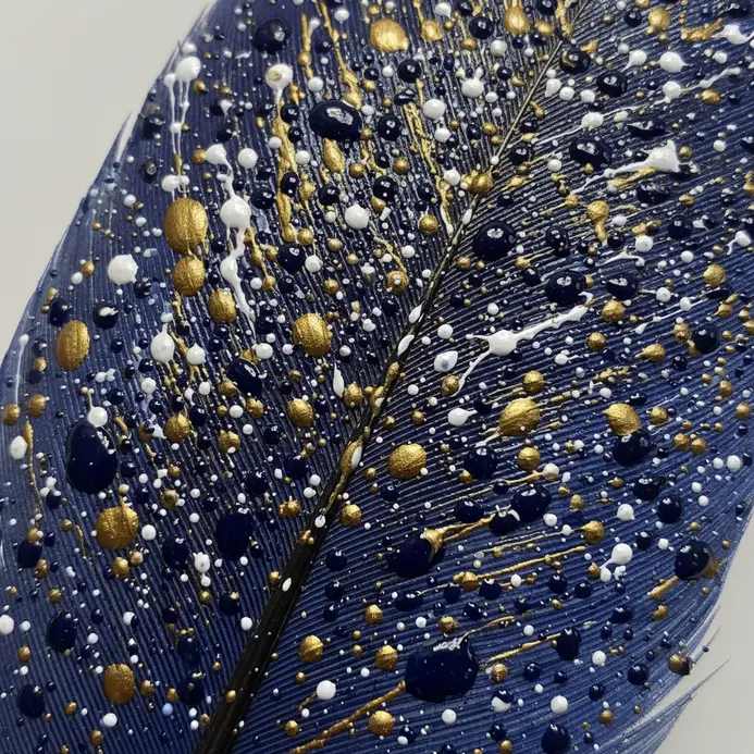 A deep blue feather with fine splatters of white and metallic gold paint resembling stars.