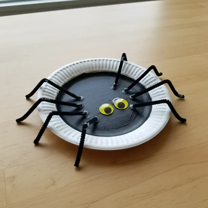 A black paper plate spider with eight bent pipe cleaner legs and large googly eyes.