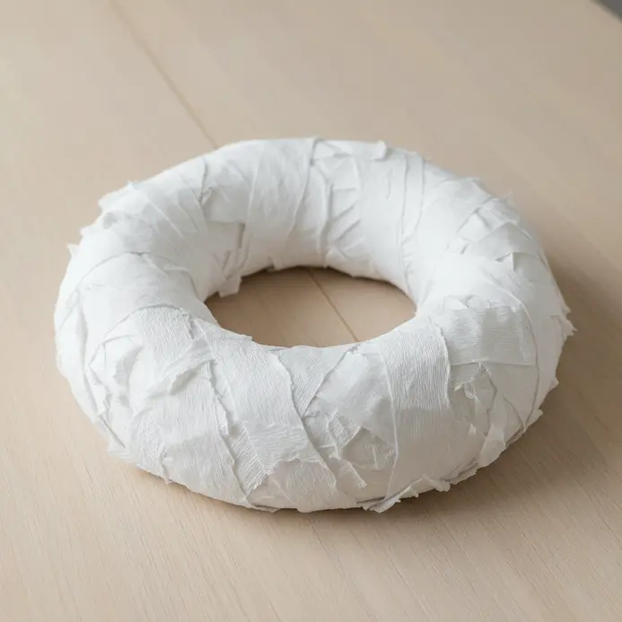 A circular wreath base completely wrapped in strips of white crepe paper to resemble bandages.