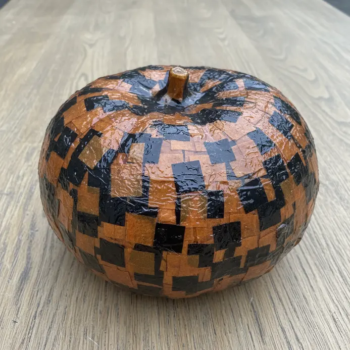 A faux pumpkin completely covered in small pieces of orange and black patterned tissue paper using decoupage glue.