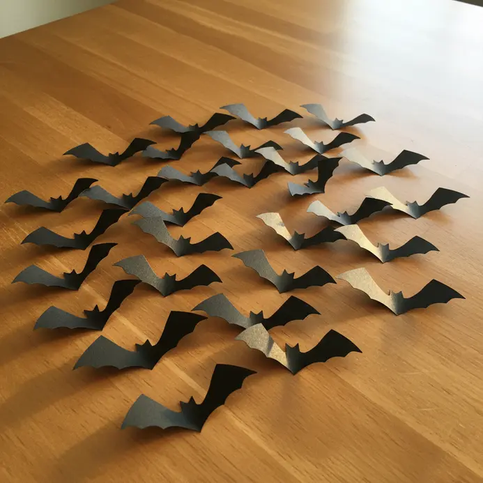 Multiple black construction paper bat silhouettes arranged in a flying swarm on a light-colored wall.