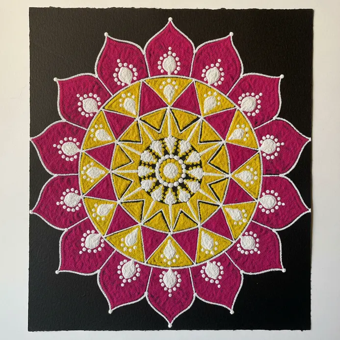 A bright, symmetrical geometric pattern created on a flat surface using vibrant colored powders or chalks.