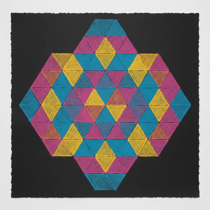 Triangular Rangoli pattern drawn with white chalk on a dark floor, filled with colored powder.