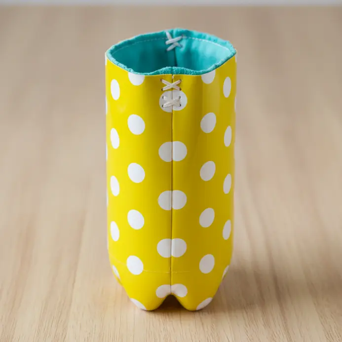 A cylindrical pencil holder made from a plastic bottle, painted with cheerful white polka dots.