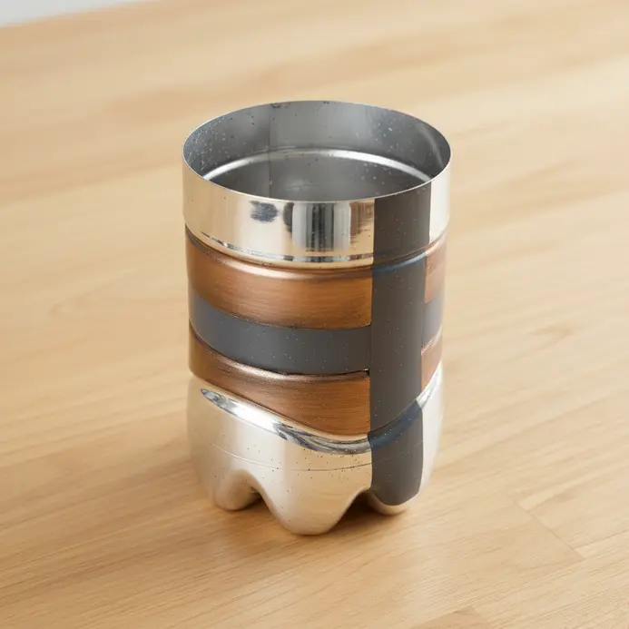 A simple desktop organizer made from a plastic bottle painted with silver or gold metallic spray paint.