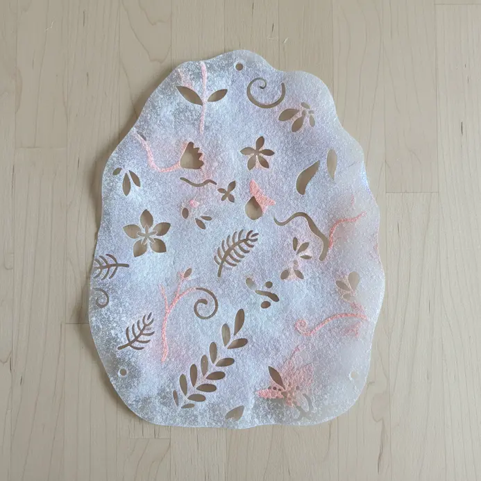 A translucent plastic sun catcher with frosted floral patterns hanging in a window.